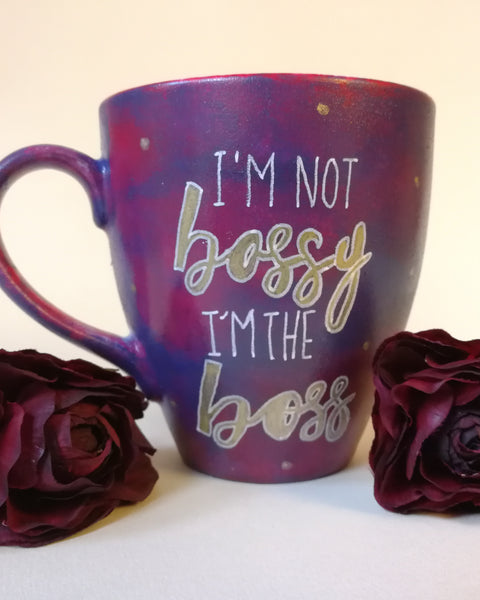 A reddish purple hand painted mug with the words "I'm not bossy , I'm the boss" with the words boss in gold and gold dots scattered all over