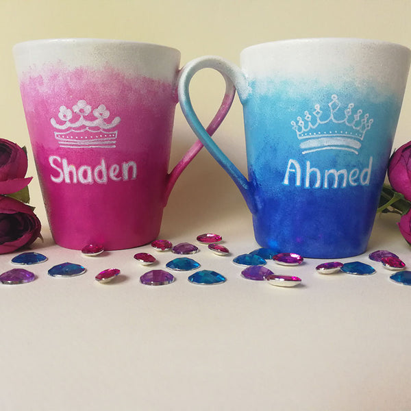 2 hand-painted mugs. One with gradients of pink and has the name "Shaden" and a crown drawn above the name and the other is colored in gradients of blue and has the name "Ahmed" and a crown drawn above the name