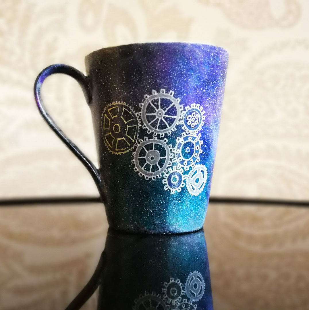 A Bluish Galaxy mug with gears painted on it in grey