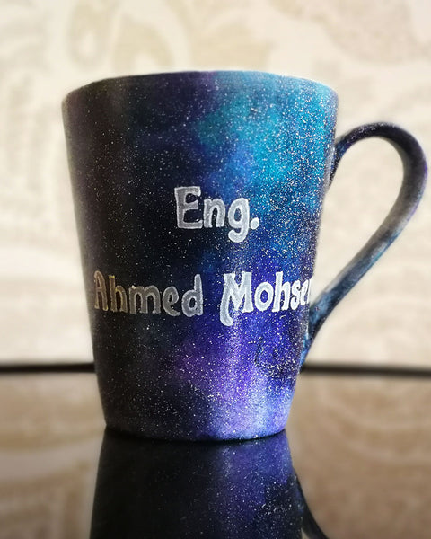 a bluish galaxy hand painted mug with the words "Eng. Ahmed Mohsen"