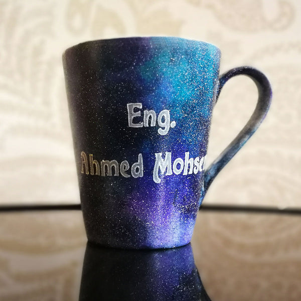 a bluish galaxy hand painted mug with the words "Eng. Ahmed Mohsen"