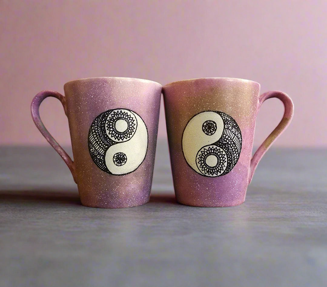 2 Hand-Painted mugs colored in pastel pinks and oen has a yin drwn on it and the other has a yang drawn on it