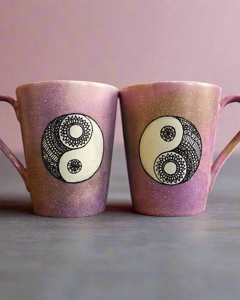 2 Hand-Painted mugs colored in pastel pinks and oen has a yin drwn on it and the other has a yang drawn on it