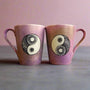 2 Hand-Painted mugs colored in pastel pinks and oen has a yin drwn on it and the other has a yang drawn on it