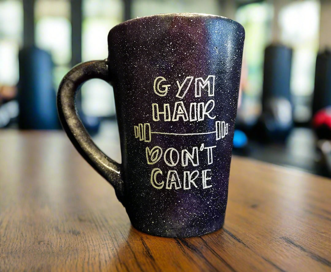 A black galaxy mug with the words "Gym hair, don't care" and a weight bar in between