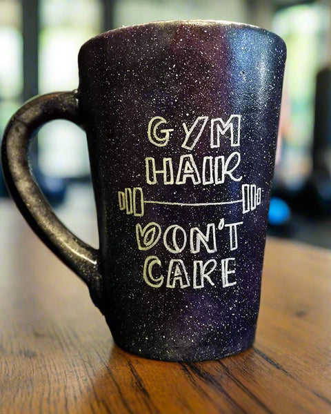 A black galaxy mug with the words "Gym hair, don't care" and a weight bar in between