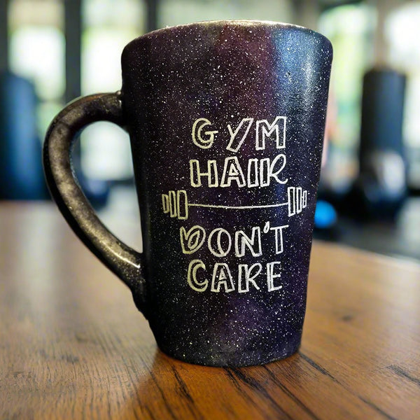 A black galaxy mug with the words "Gym hair, don't care" and a weight bar in between