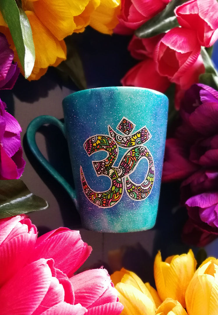 A Blue Galaxy hand painted mug with an om painted in white and filled with colorful doodles