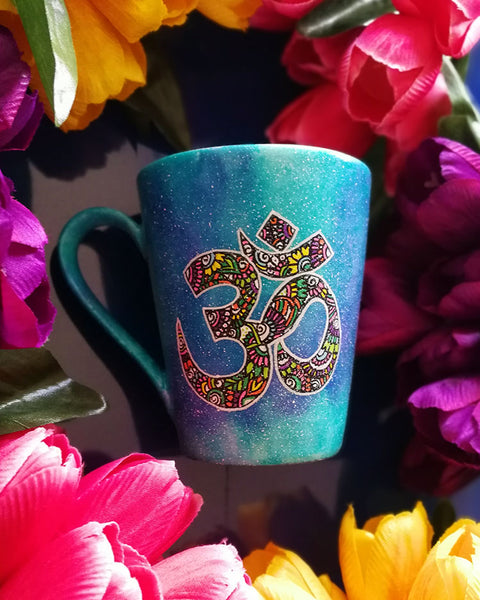 A Blue Galaxy hand painted mug with an om painted in white and filled with colorful doodles