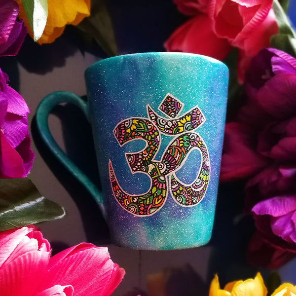 A Blue Galaxy hand painted mug with an om painted in white and filled with colorful doodles