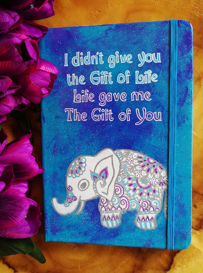 A Blue hand painted notebook with the words "I didnt give you the fit of life, Life gave me the gift of you" and a n elephant drawn below it in white and filled with patterns