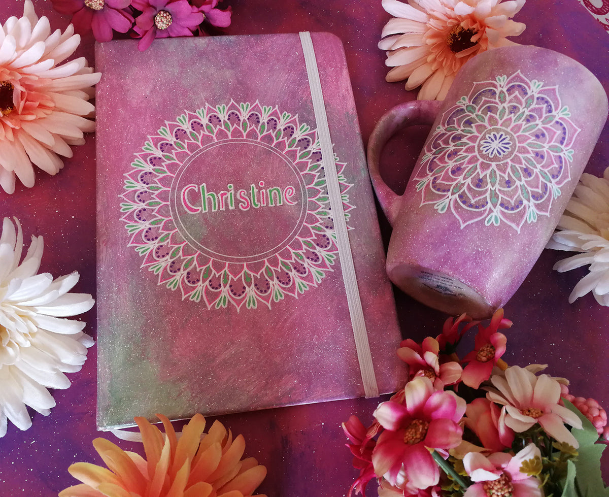 A gift set of mug and notebook in pastel pink , both with mandalas. and the notebook has the name christine inside the mandala