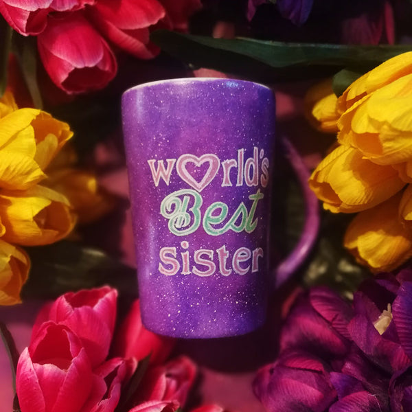 A Purple galaxy hand painted mug with the sentence "Worlds best sister" written in white and colored in with pink and green