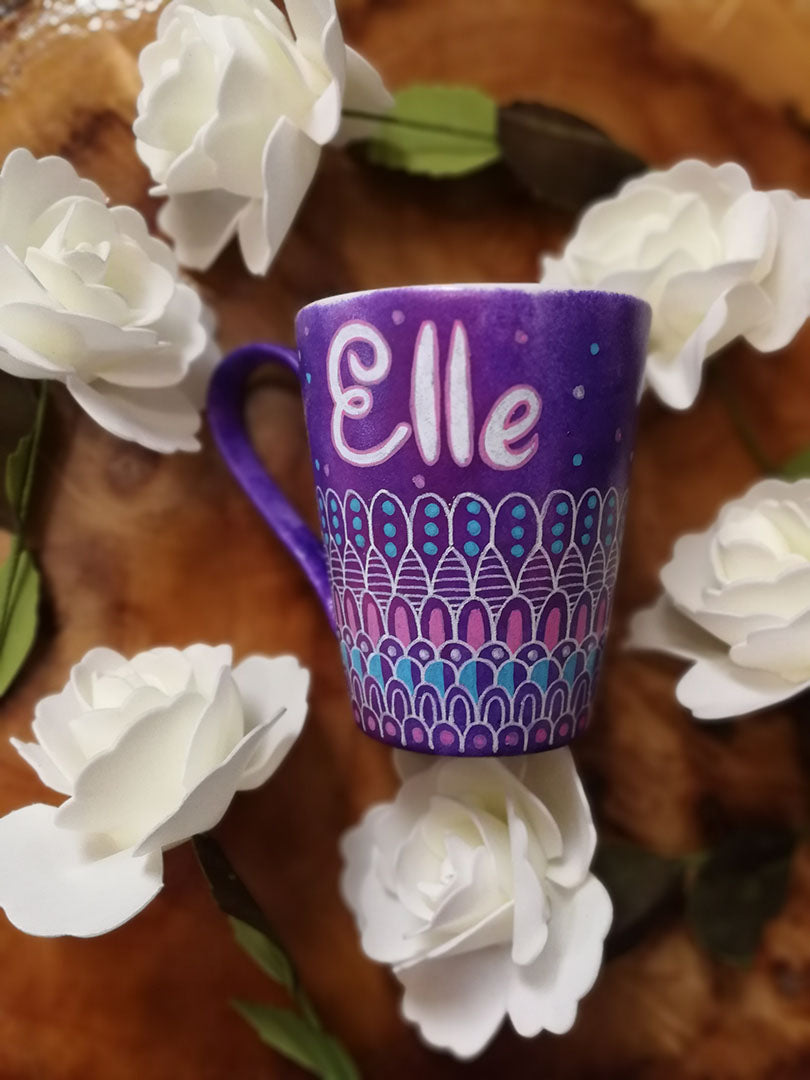 A Purple hand painted mug with patterns on the bottom half horizontally in white and colored in pink and blue with the name "Elle" on the top