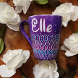 A Purple hand painted mug with patterns on the bottom half horizontally in white and colored in pink and blue with the name 