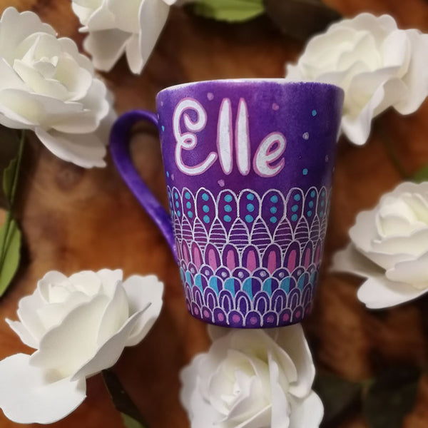 A Purple hand painted mug with patterns on the bottom half horizontally in white and colored in pink and blue with the name "Elle" on the top