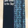 A Dark Blue Notebook with patterns drawn Vertically on half of the notebook top down and the the half has the words "your limit is the sky"