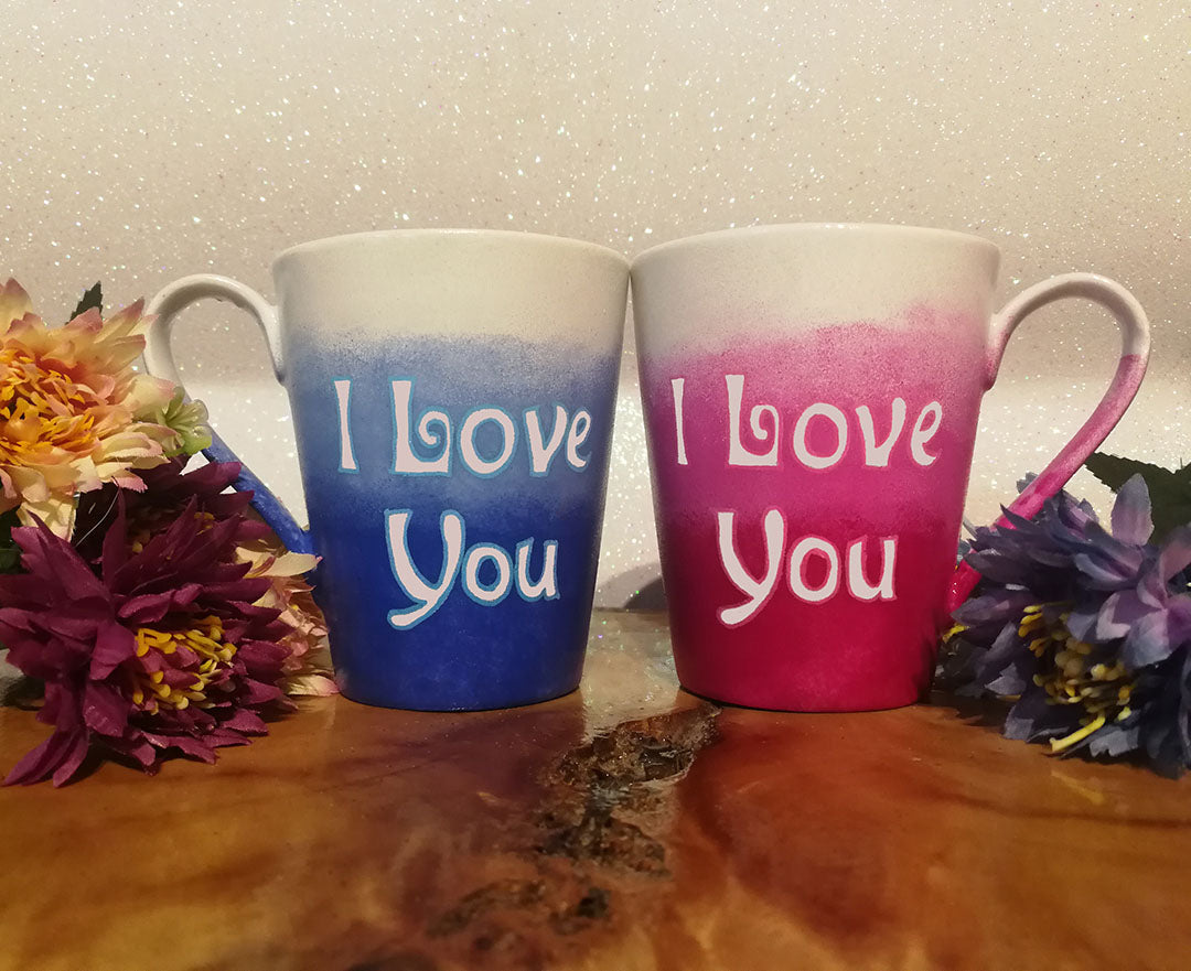 2 hand-painted mugs. one colored in gradient blues to white and has the words I love you on it. the other is colored in gradient pinks to white and has the words I love you on it