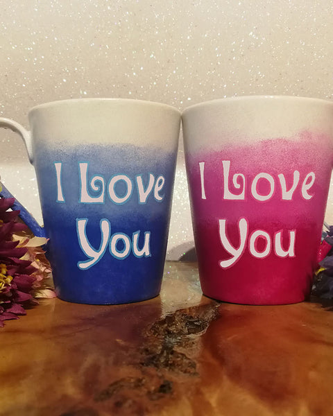 2 hand-painted mugs. one colored in gradient blues to white and has the words I love you on it. the other is colored in gradient pinks to white and has the words I love you on it