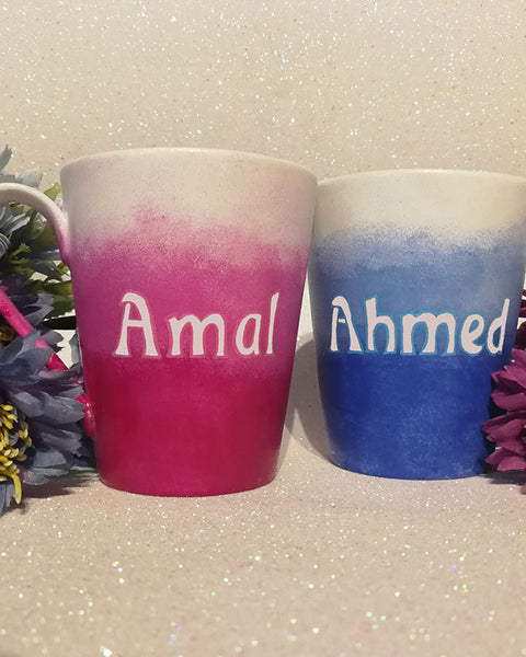 2 hand-painted mugs. one colored in gradient blues to white and has the name "ahmed". the other is colored in gradient pinks to white and has the name "Amal" on it