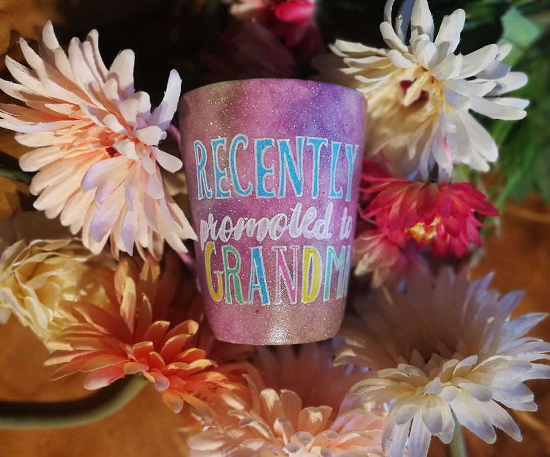 A Pastel Pink Hand painted mug with the words "Recently promoted to Grandma" written in white and colored in with blue, pale pink, yellow and geen