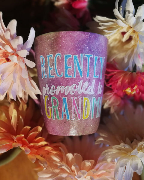 A Pastel Pink Hand painted mug with the words "Recently promoted to Grandma" written in white and colored in with blue, pale pink, yellow and geen