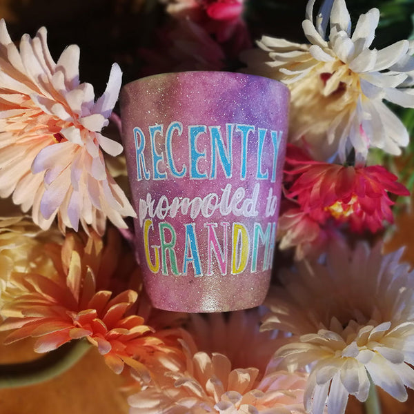 A Pastel Pink Hand painted mug with the words "Recently promoted to Grandma" written in white and colored in with blue, pale pink, yellow and geen