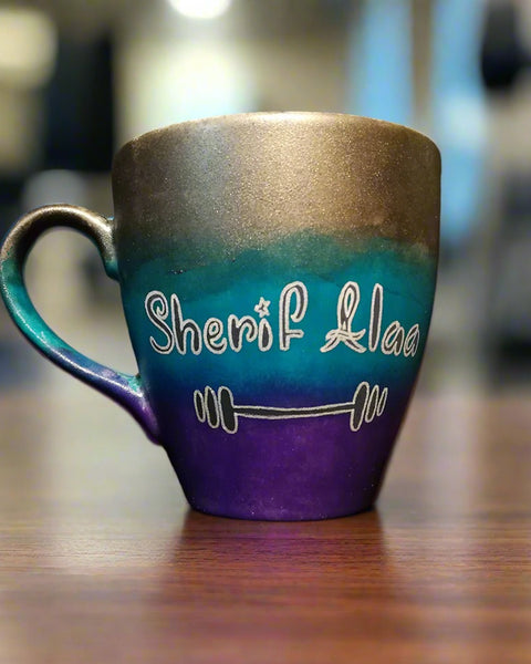 A gradient colored mug (Silver, turquoise and purple) with the name "Sherif Alaa"and a small weight bar drawn below it