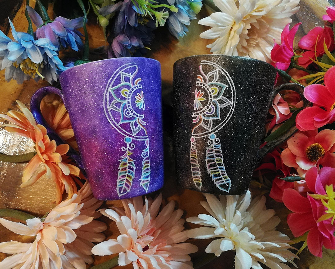 Two Hand-painted mugs one in purple galaxy color and the other black galaxy color  with a dreamcatcher divided in two , one on each mug