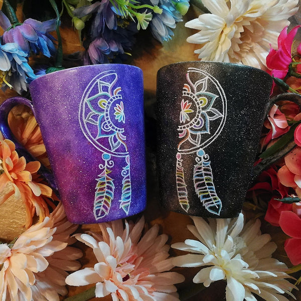 Two Hand-painted mugs one in purple galaxy color and the other black galaxy color  with a dreamcatcher divided in two , one on each mug