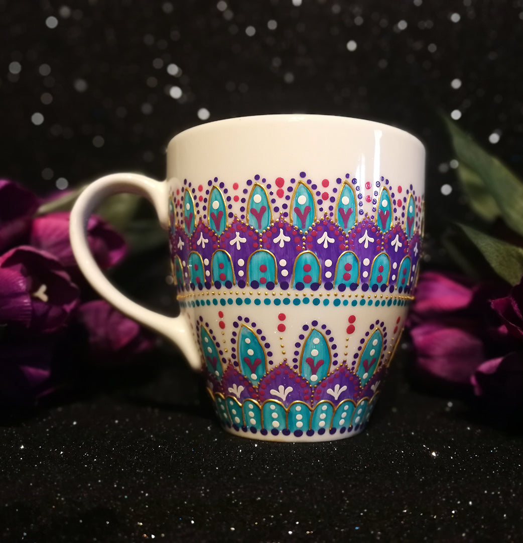 A White mug with patterns in purple and turquoise outlined with gold relief and dot art of white purple pink and turquoise