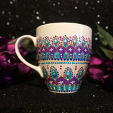 A White mug with patterns in purple and turquoise outlined with gold relief and dot art of white purple pink and turquoise