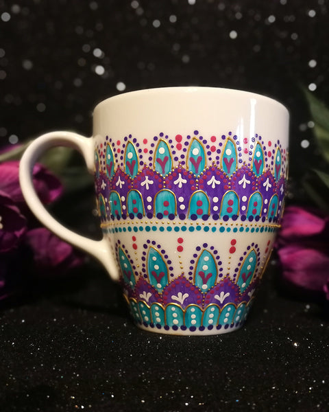 A White mug with patterns in purple and turquoise outlined with gold relief and dot art of white purple pink and turquoise