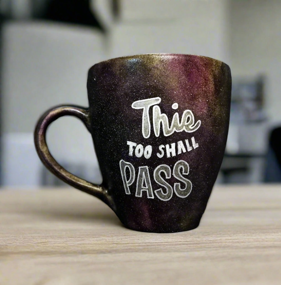 A Black galaxy mug with the words "this too shall pass"