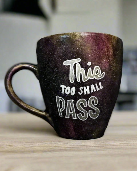 A Black galaxy mug with the words "this too shall pass"