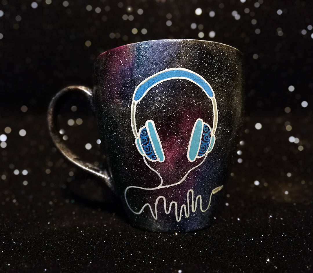 A Black galaxy hand painted mug with a headset design on it