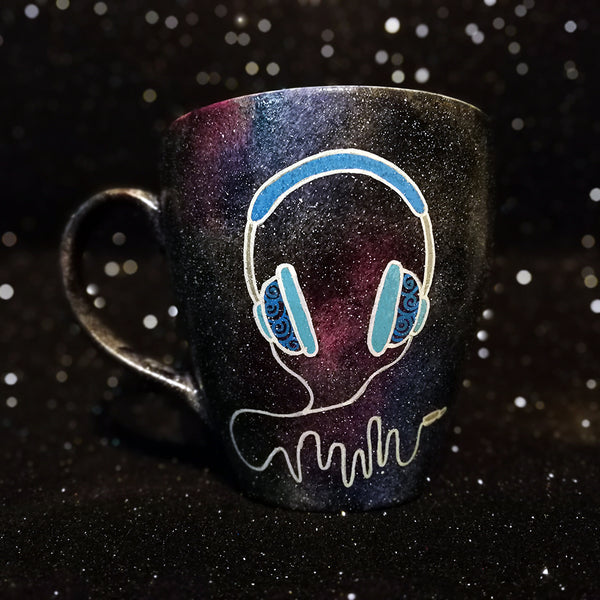 A Black galaxy hand painted mug with a headset design on it