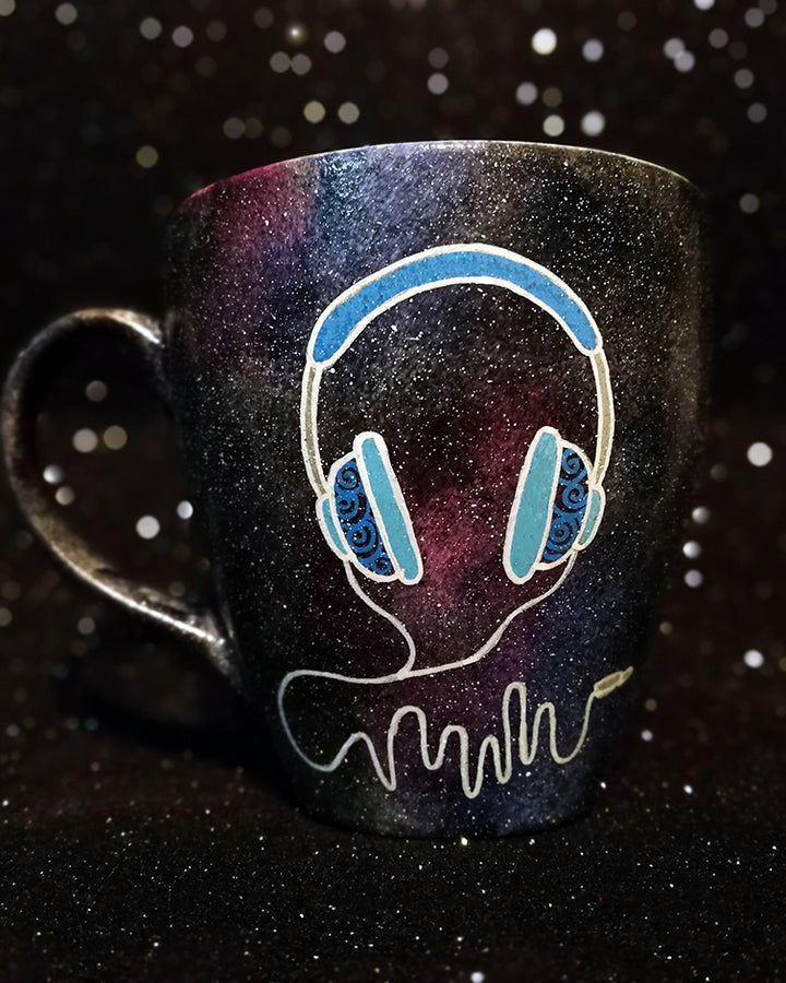 A Black galaxy hand painted mug with a headset design on it