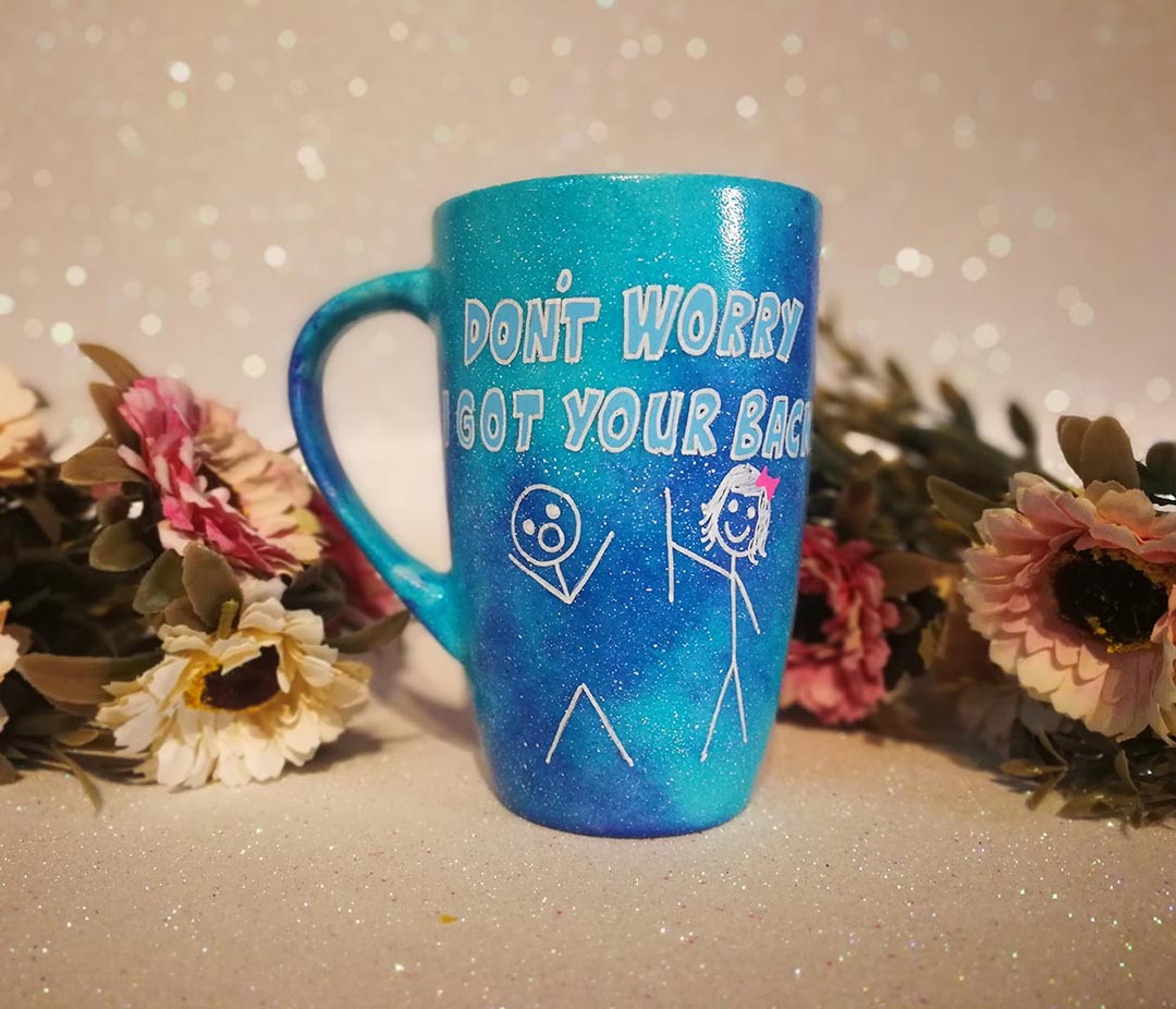 A hand painted blue galaxy mug with the words "don't worry, I got your back " and a drawing of 2 stick figures with the girl holding the back of the boy