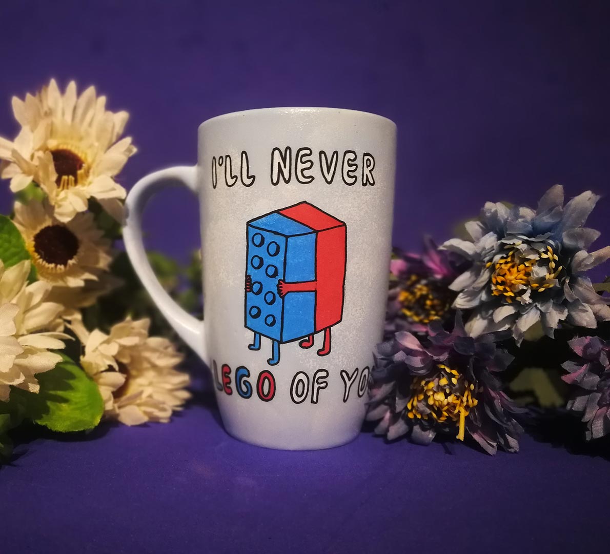 A baby blue hand-painted mug with the words "I'll never" and below it two lego pieces hugging each other and the below it the words "LEGO of you"