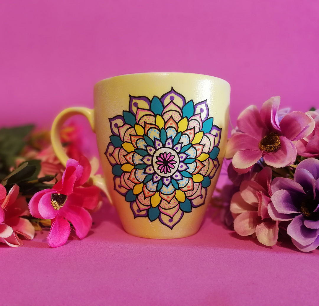 A Pastel yellow hand painted mug with a mandala drawn in black and colored in pink, purple, yellow, orange , teal and blue