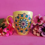 A Pastel yellow hand painted mug with a mandala drawn in black and colored in pink, purple, yellow, orange , teal and blue