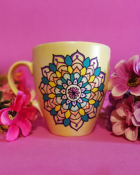 A Pastel yellow hand painted mug with a mandala drawn in black and colored in pink, purple, yellow, orange , teal and blue