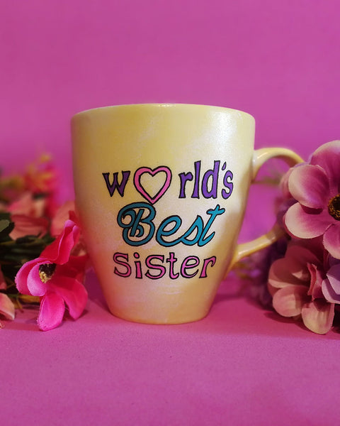 A Pastel yellow hand painted mug with the sentence "Worlds best Sister" written in black and colored in purple , pink and turquoise