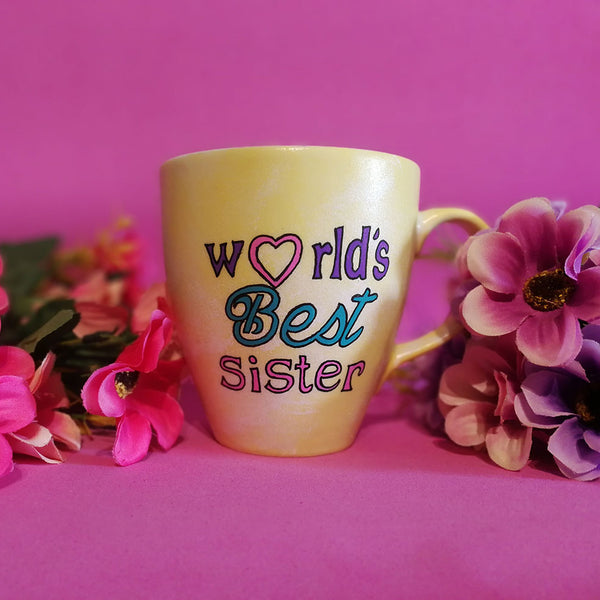 A Pastel yellow hand painted mug with the sentence "Worlds best Sister" written in black and colored in purple , pink and turquoise