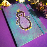 a Blue galaxy hand painted notebook with a penguin painted on it