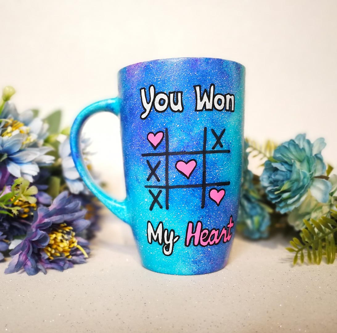 A hand painted blue galaxy mug with the sentence "you won" and under it an x o chart with hearts instead of o  and three hearts winning the game diagonally, then under it the words "My heart"