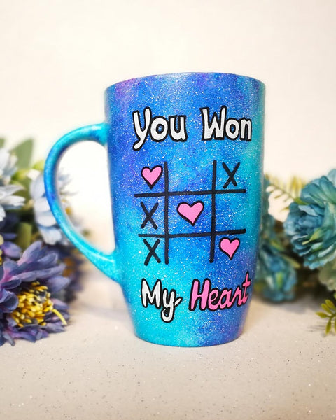 A hand painted blue galaxy mug with the sentence "you won" and under it an x o chart with hearts instead of o  and three hearts winning the game diagonally, then under it the words "My heart"