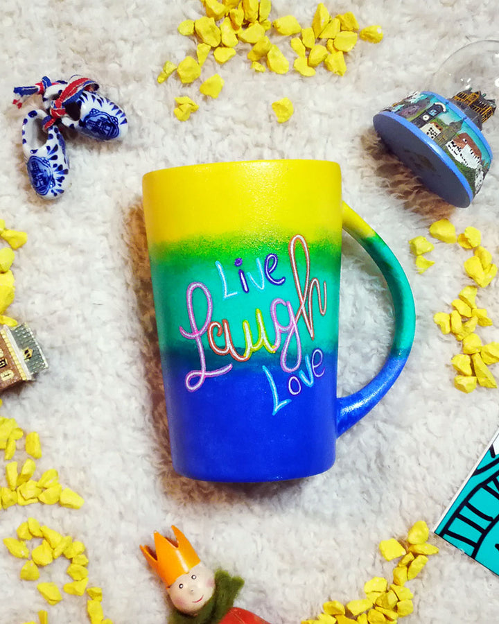 A gradient Hand Painted mug (from the top yellow, green,blue) with the words Live Laugh Love