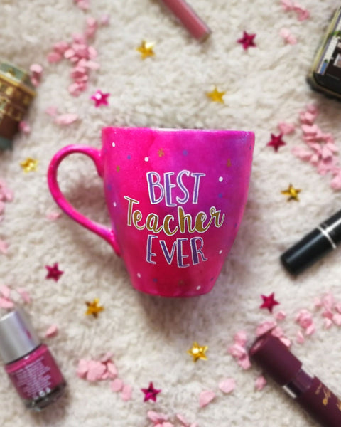 A indian pink hand painted mug with the words "Best teacher Ever" where Best and ever words are in purple and teacher is written in cursive in gold